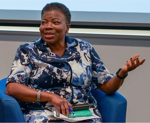 Dr. Funke Oba sits in chair, holding a microphone at an event.